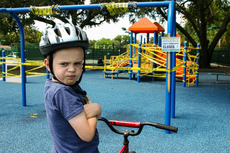 Kind mit Fahrradhelm schaut trotzig auf einem Spielplatz