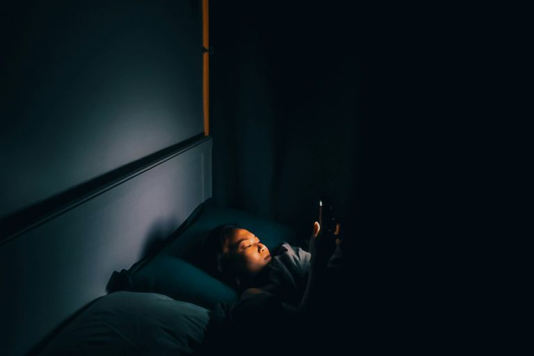 Eine Person liegt nachts wach im dunklen Schlafzimmer und schaut auf ihr Handy